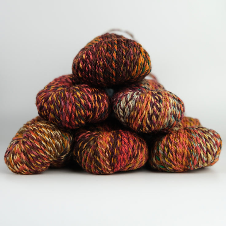 An image of skeins of Spincycle Dream State worsted weight yarn in a red, orange, gray blue, and brown color gradient against a gray background.