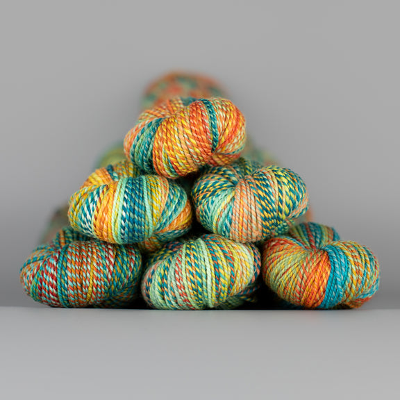 Skeins of Spincycle Dyed in the Wool sport weight yarn in a blue, green, orange, and yellow color gradient against a gray background.
