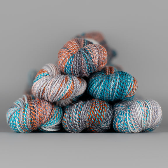 Skeins of Spincycle Dyed in the Wool sport weight yarn in a blue, orange, gray, and purple color gradient against a gray background.