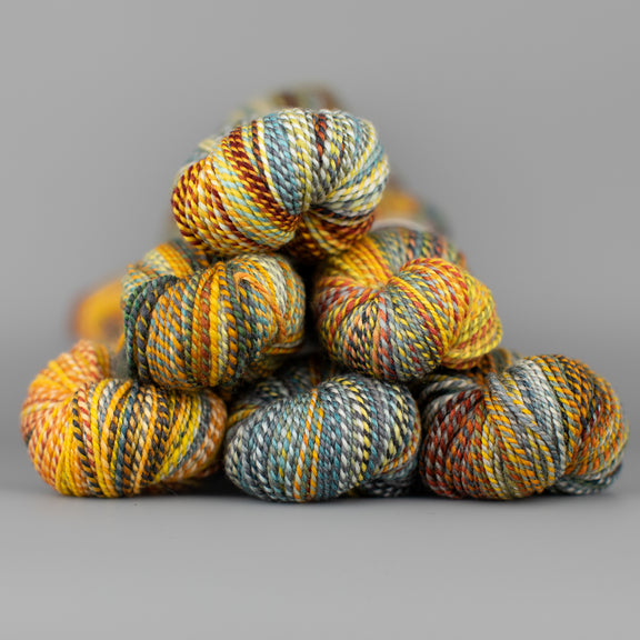 Skeins of Spincycle Dyed in the Wool sport weight yarn in a yellow, red, gray, and pale blue color gradient against a gray background.