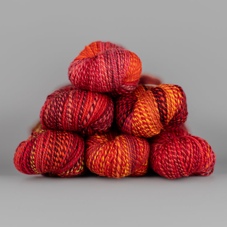 Skeins of Spincycle Dyed in the Wool sport weight yarn in a red, maroon, orange, and yellow color gradient against a gray background.