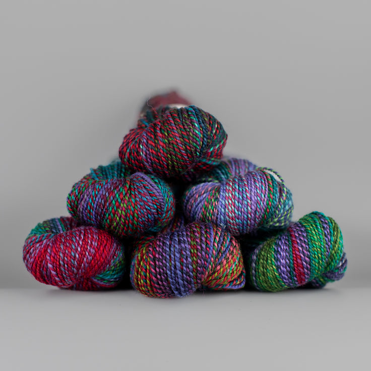 Skeins of Spincycle Dyed in the Wool sport weight yarn in a blue, green, red, and purple color gradient against a gray background.