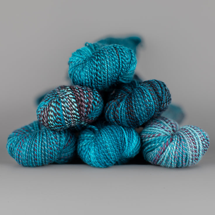 Skeins of Spincycle Dyed in the Wool sport weight yarn in a bright blue, navy, and purple color gradient against a gray background.