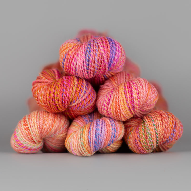 Skeins of Spincycle Dyed in the Wool sport weight yarn in a pink, orange, and purple color gradient against a gray background.