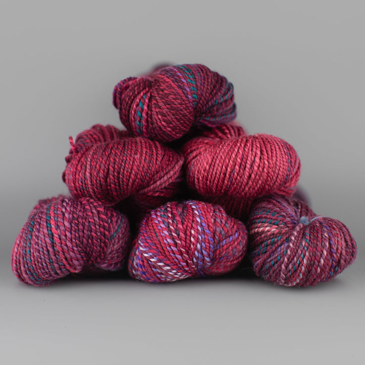 Skeins of Spincycle Dyed in the Wool sport weight yarn in a magenta, purple, and blue color gradient against a gray background.