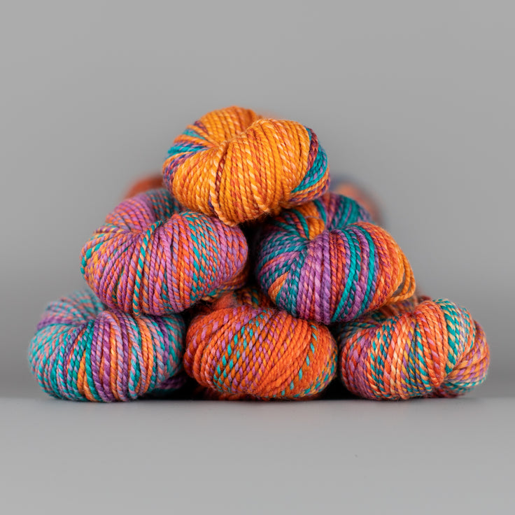 Skeins of Spincycle Dyed in the Wool sport weight yarn in an orange, blue, and purple pink color gradient against a gray background.