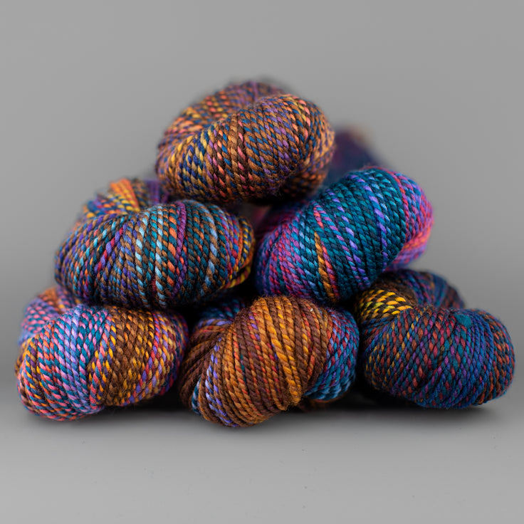 Skeins of Spincycle Dyed in the Wool sport weight yarn in a blue, brown, orange, and purple color gradient against a gray background.