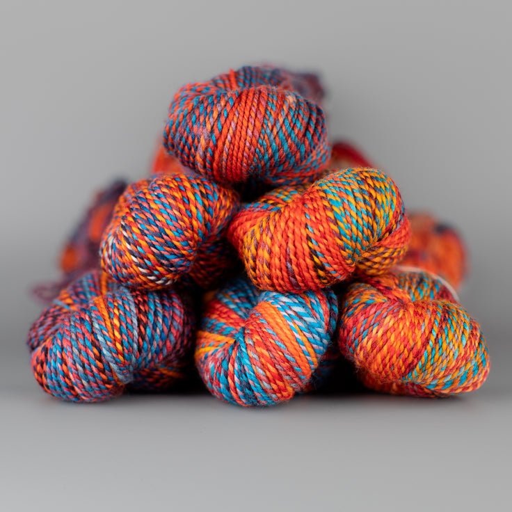 Skeins of Spincycle Dyed in the Wool sport weight yarn in a blue, orange, and red color gradient against a gray background.