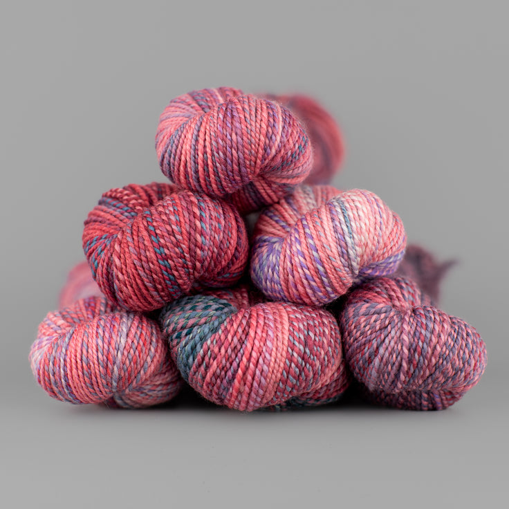 Skeins of Spincycle Dyed in the Wool sport weight yarn in a pink, purple, and blue gray color gradient against a gray background.