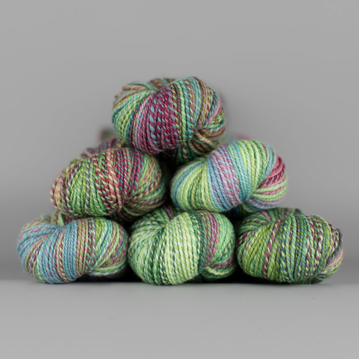 Skeins of Spincycle Dyed in the Wool sport weight yarn in a green, blue, and maroon color gradient against a gray background.