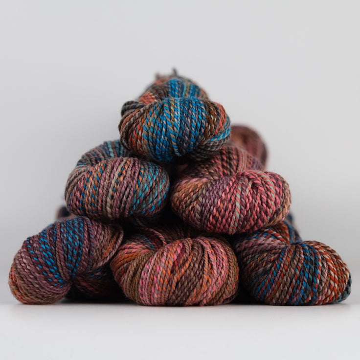 Skeins of Spincycle Dyed in the Wool sport weight yarn in a blue, brown, red orange, and mauve color gradient against a gray background.